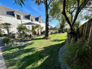 A residential property with a well-maintained lawn, a variety of plants, and a large tree in the center.
