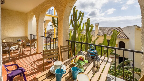 A balcony with a table set for breakfast, surrounded by cacti and a view of a traditional building. - Beautiful apartment in Mijas with swimming pool (Mijas)