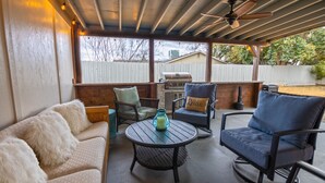 A covered patio with a grill, seating area, and a ceiling fan.