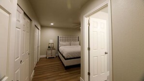 A narrow hallway with a bed at the end, a nightstand with a lamp, and a ceiling fan.