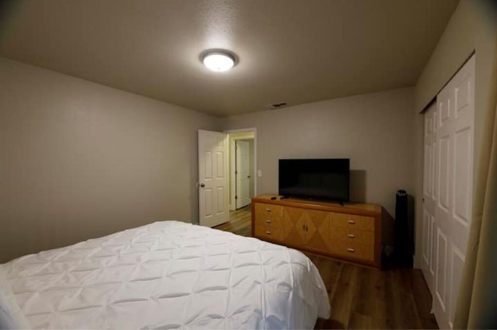 Un dormitorio con cama, cómoda, televisor y una puerta que da a otra habitación.