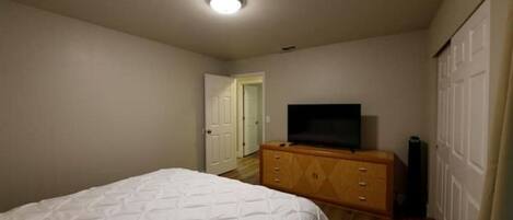 Un dormitorio con cama, cómoda, televisor y una puerta que da a otra habitación.
