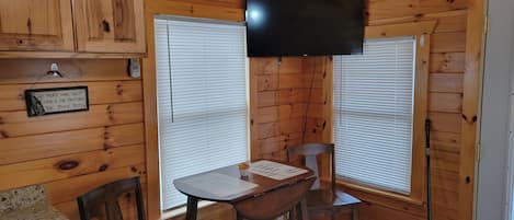 A wooden cabin interior with a dining table, chairs, a television mounted on the wall, and a sign on the wall.