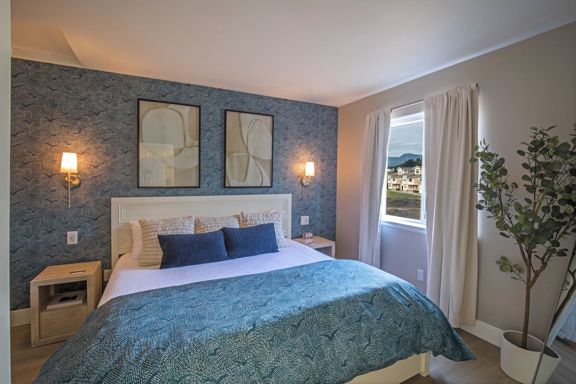 A bedroom with a bed, two wall-mounted lamps, a nightstand, a window with curtains, and a potted plant.