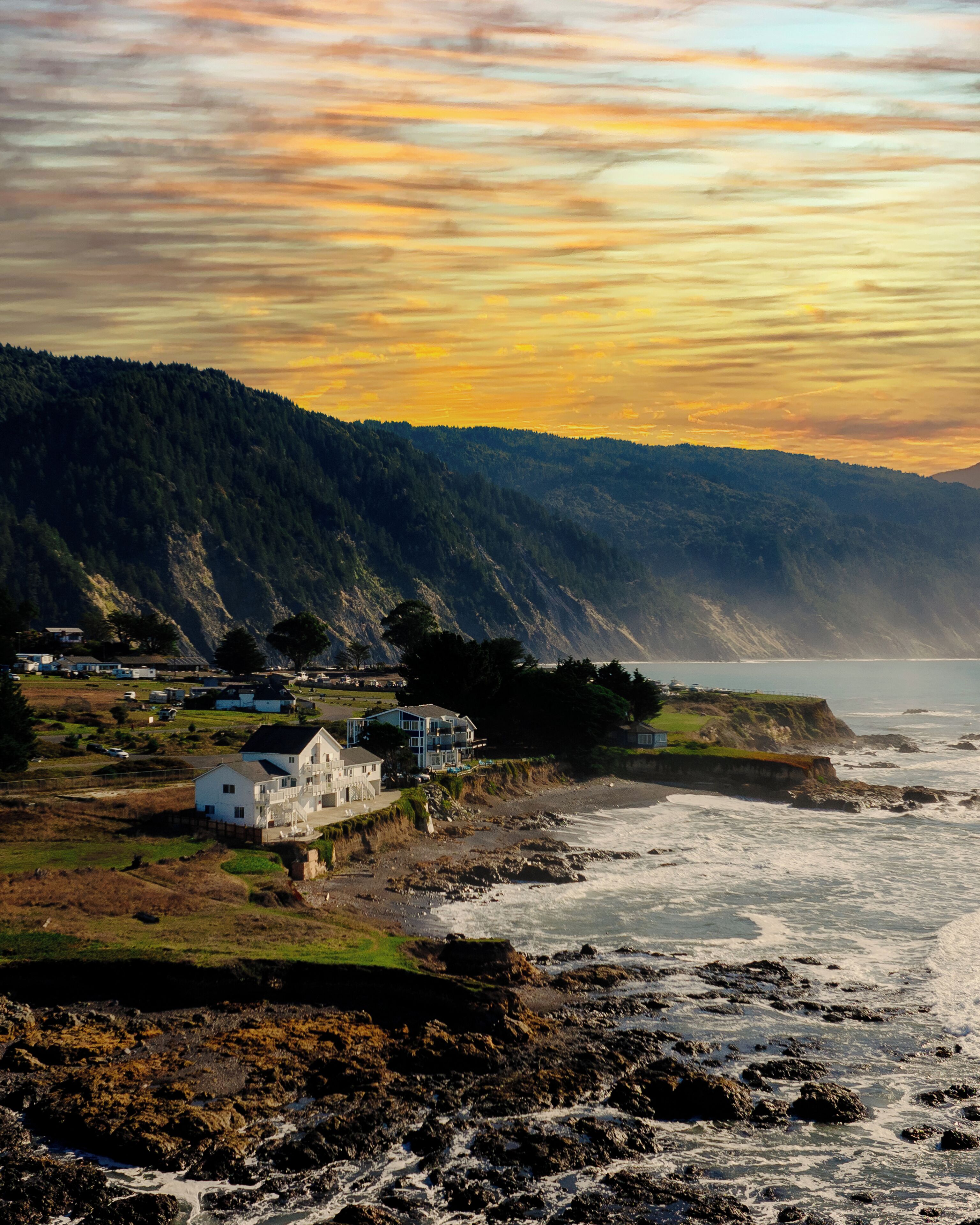 A coastal house with a view of the sea and a forested hillside.