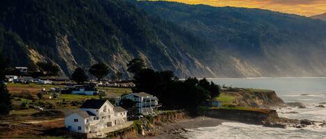 A coastal house with a view of the sea and a forested hillside.