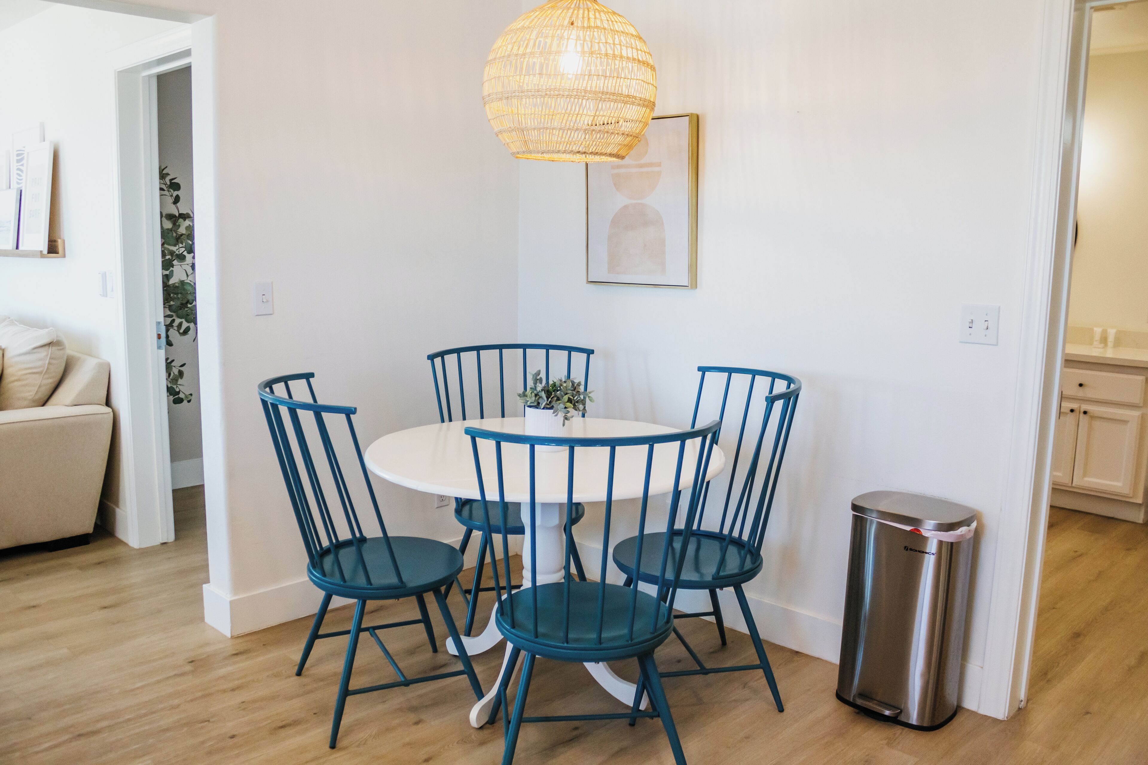 A dining area with a round table and four chairs, a trash bin, and a hanging light fixture.