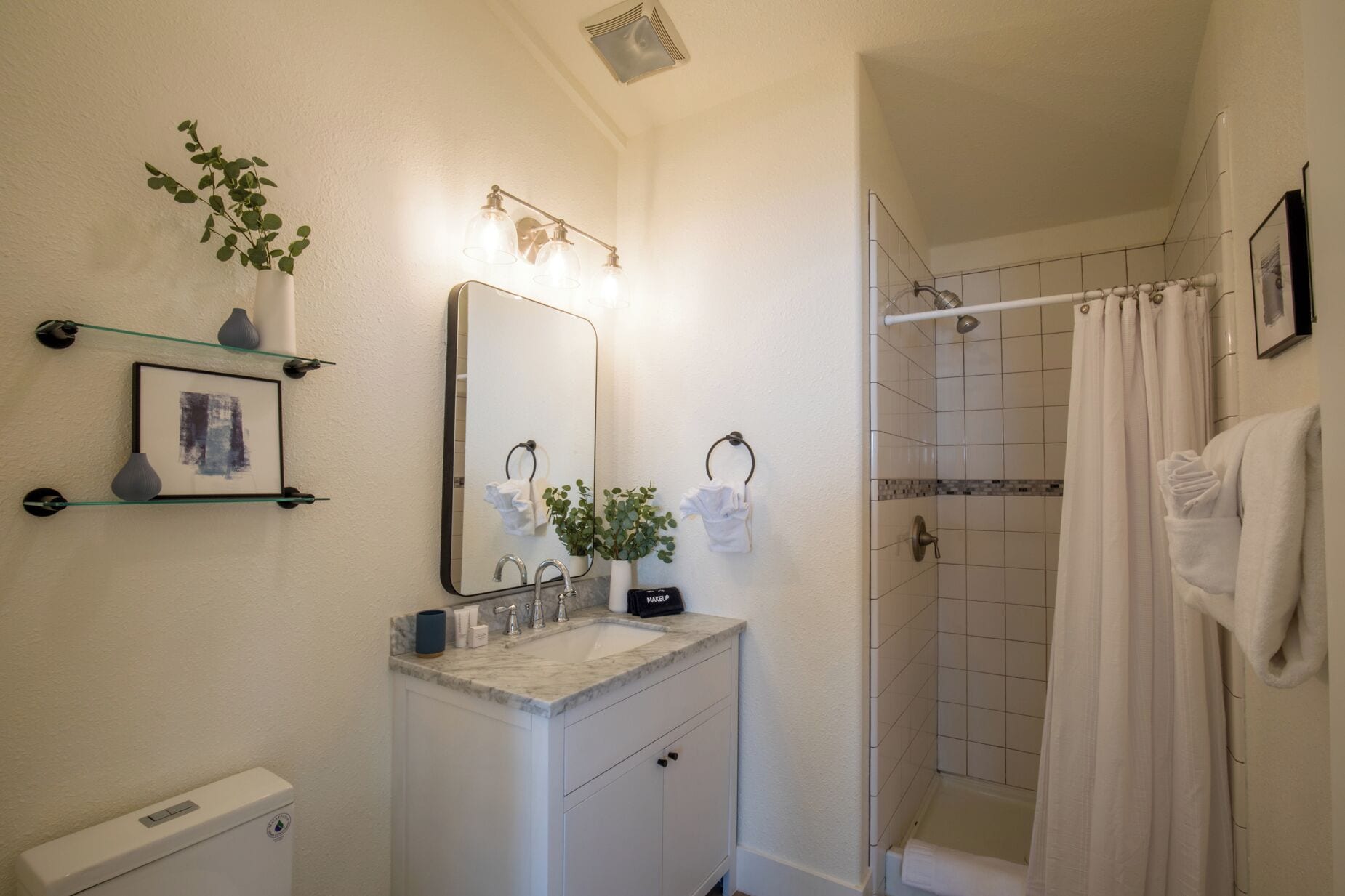 Ein Badezimmer mit Toilette, Waschbecken, Spiegel, Handtuchhalter, Dusche und einem gerahmten Bild an der Wand.