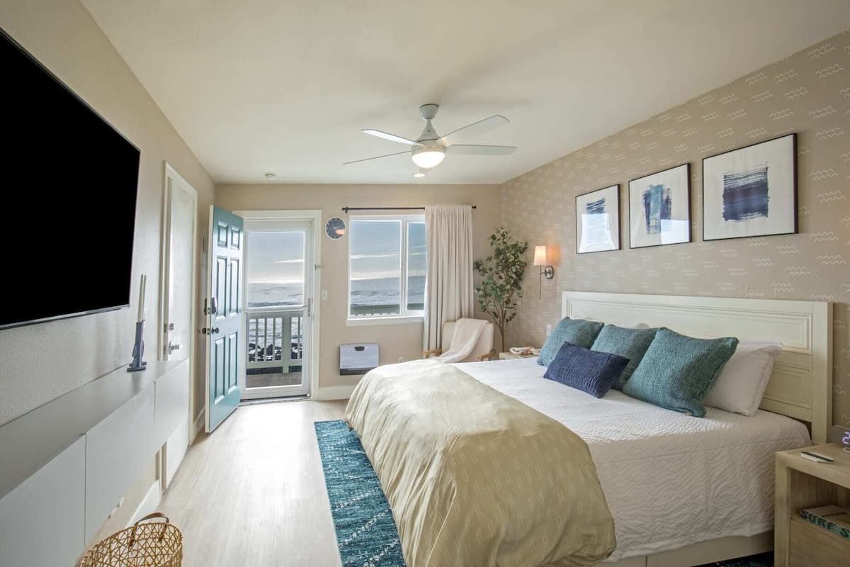 A hotel room with a bed, a ceiling fan, a view of the ocean, and a door leading to a balcony.