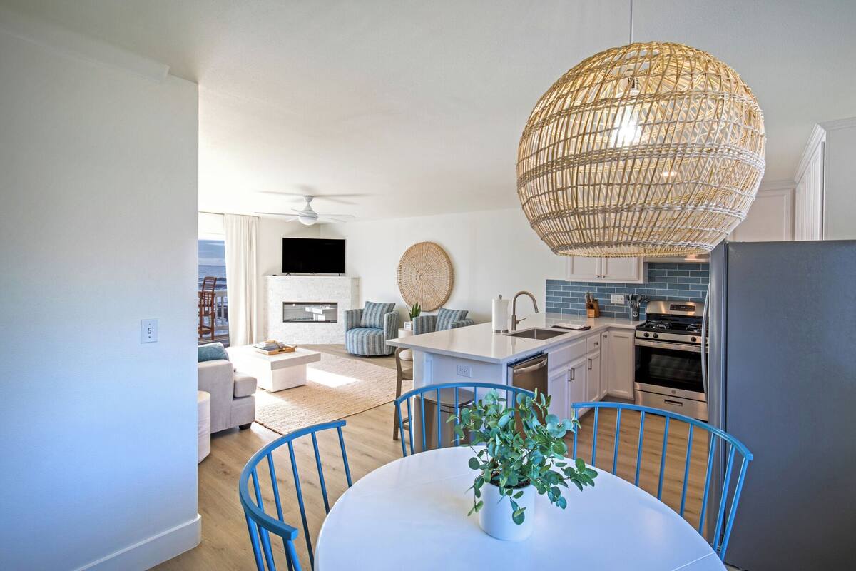 A modern kitchen with a central island, a dining area with a table and chairs, and a living room with a sofa and a television.