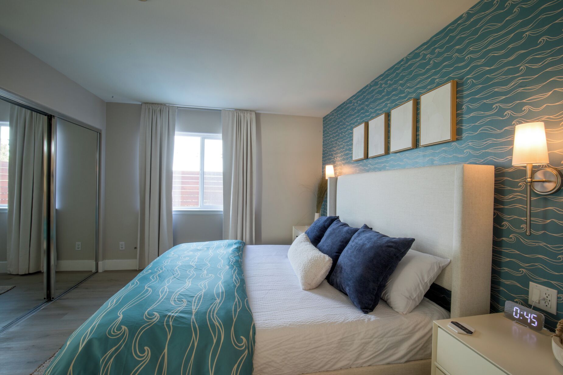 Habitación de hotel con cama, mesita de noche, reloj de pared y ventana con cortinas.