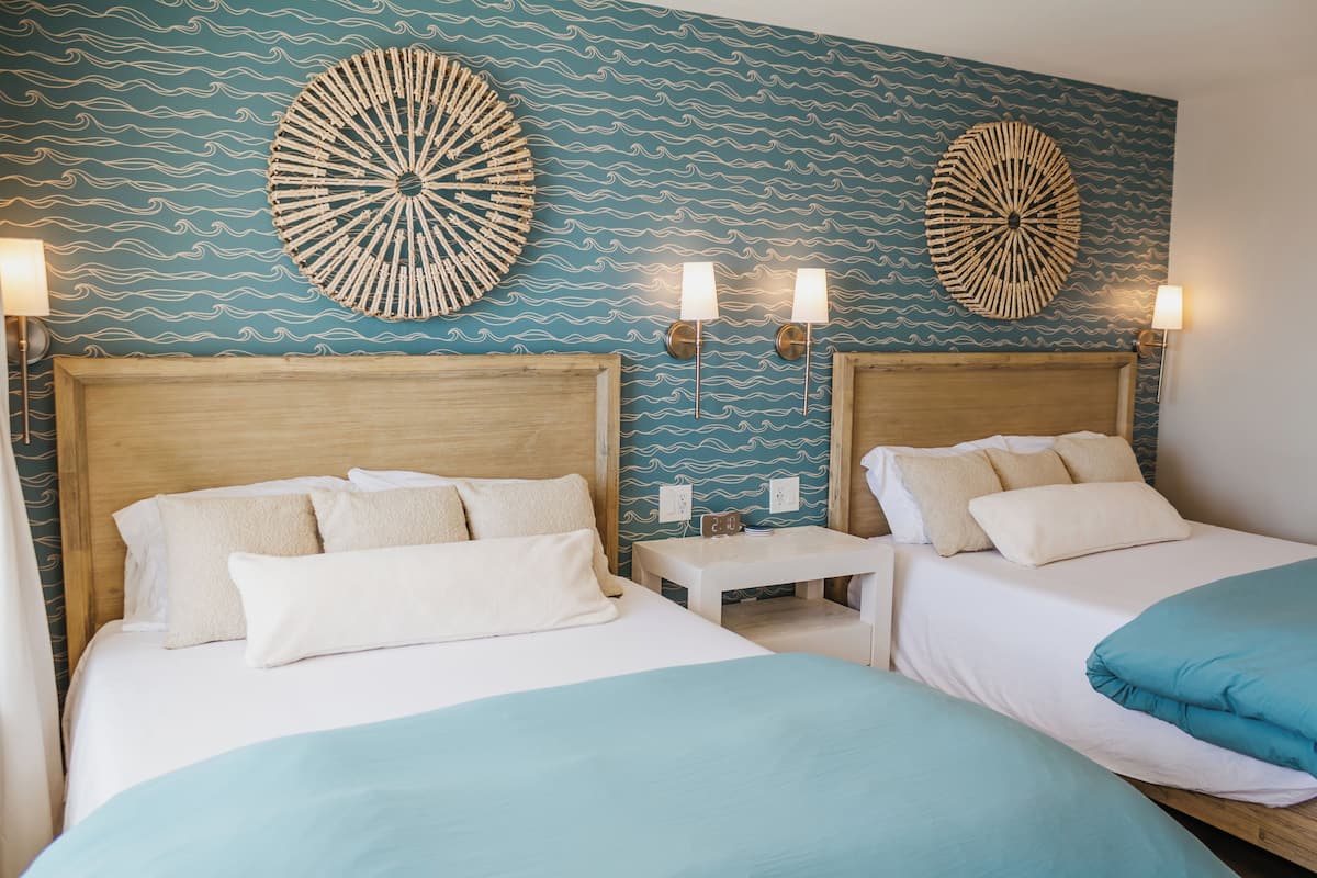 A hotel room with two beds, a wooden headboard, a small bedside table, and wall decor.