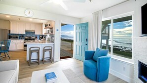 A modern kitchen with white cabinets, a central island with bar stools, and a view of the ocean through a large window. - Black Sands Inn (Shelter Cove)