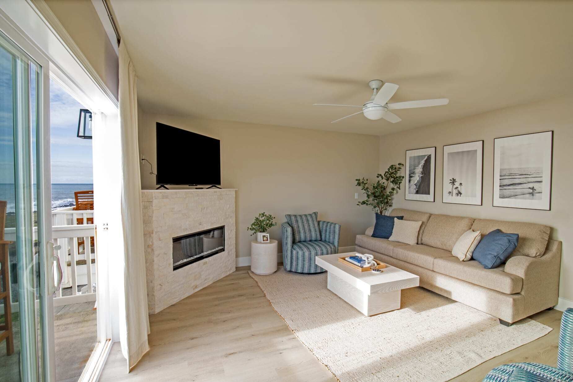 Un salon avec une cheminée, un canapé, une table basse et un téléviseur fixé au-dessus de la cheminée. Les murs sont ornés de tableaux encadrés et le plafond est équipé d’un ventilateur.