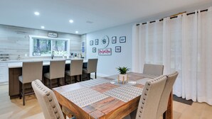 Een moderne eethoek met een houten tafel, beige stoelen en een keuken op de achtergrond.