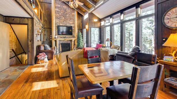 Un interior acogedor con chimenea de piedra, mobiliario de madera y grandes ventanas que ofrecen vistas al exterior.