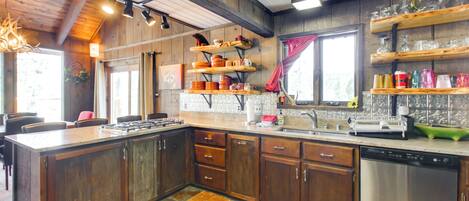 A kitchen with wooden cabinets, a stainless steel dishwasher, and shelves with kitchenware.