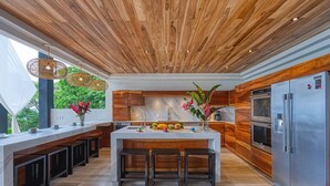 A modern kitchen with a wooden ceiling, a central island with stools, and stainless steel appliances. - BEAUTY OF COSTA RICA STUNNING VIEW (Uvita)