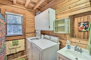 Ein Badezimmer einer Holzhütte mit Waschmaschine, Waschbecken und einem Fenster mit Jalousien.