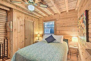 Ein Schlafzimmer einer Holzhütte mit Bett, Fenster, Deckenventilator und Wandlampe.