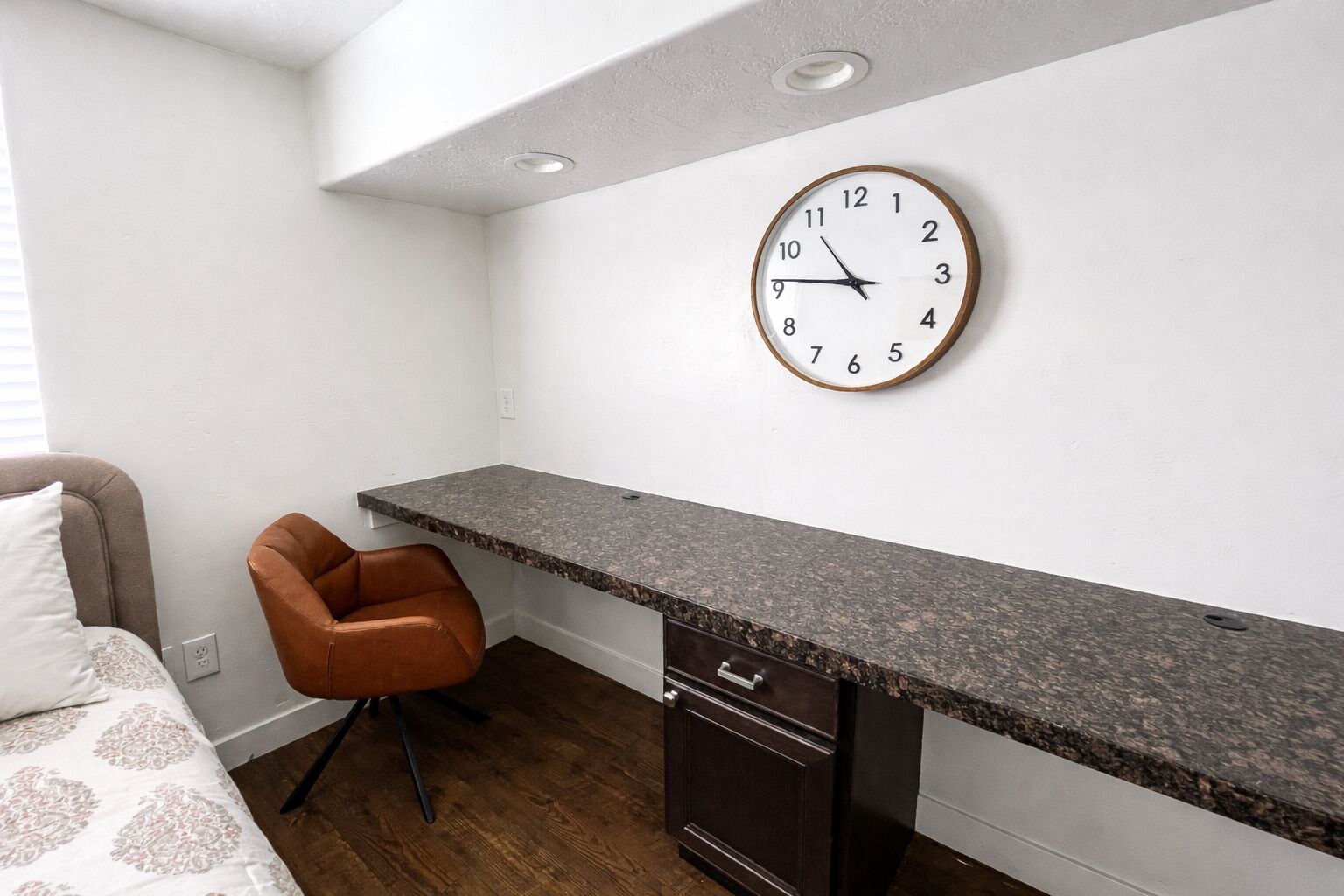 Une petite pièce moderne comprenant un comptoir de cuisine, un fauteuil en cuir marron, un four encastré et une horloge murale.