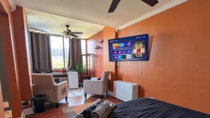 Ein Hotelzimmer mit Bett, Wandfernseher, Schreibtisch mit Stuhl und Blick ins Freie durch ein Fenster.