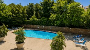 Ein Pool mit Liegestühlen und Topfpflanzen, umgeben von einer Ziegelmauer und Bäumen.