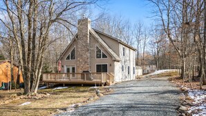 A two-story house with a stone chimney, a wooden deck, and a gravel driveway. - Charming Towamensing Trails Chalet - Sleeps 9, Fireplace, BBQ Deck & Large Yard (Albrightsville)