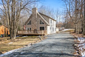 A two-story house with a stone chimney, a wooden deck, and a gravel driveway.