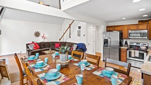 A modern kitchen with stainless steel appliances, wooden cabinets, and a dining area with blue tableware. - Charming Towamensing Trails Chalet - Sleeps 9, Fireplace, BBQ Deck & Large Yard (Albrightsville)