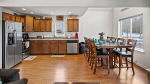 A spacious kitchen with wooden cabinets, a stainless steel refrigerator, and a dining area with a wooden table and chairs. - Charming Towamensing Trails Chalet - Sleeps 9, Fireplace, BBQ Deck & Large Yard (Albrightsville)