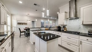 Una cucina moderna con mobili bianchi, un'isola centrale, elettrodomestici in acciaio inossidabile e lampade a sospensione.