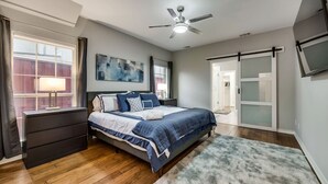 Quarto com cama, mesa de cabeceira, luminária, ventilador de teto e vista para o exterior.