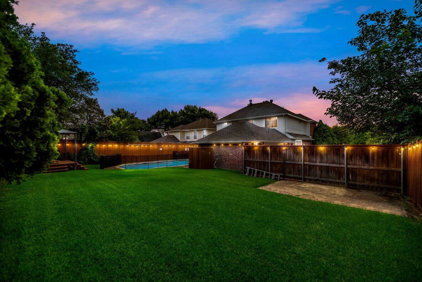 A backyard with a swimming pool, wooden fence, and string lights.