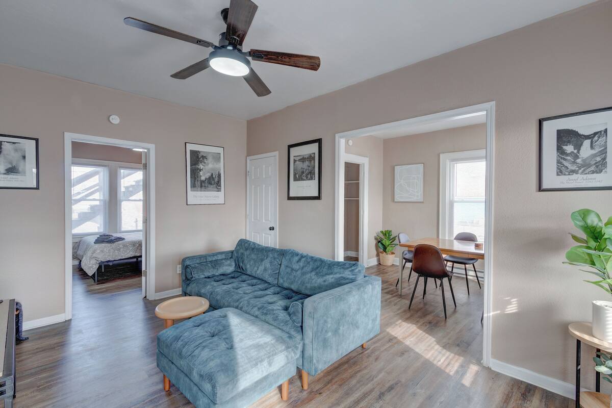 A spacious living room with a sectional sofa, a dining area with a table and chairs, and a ceiling fan.