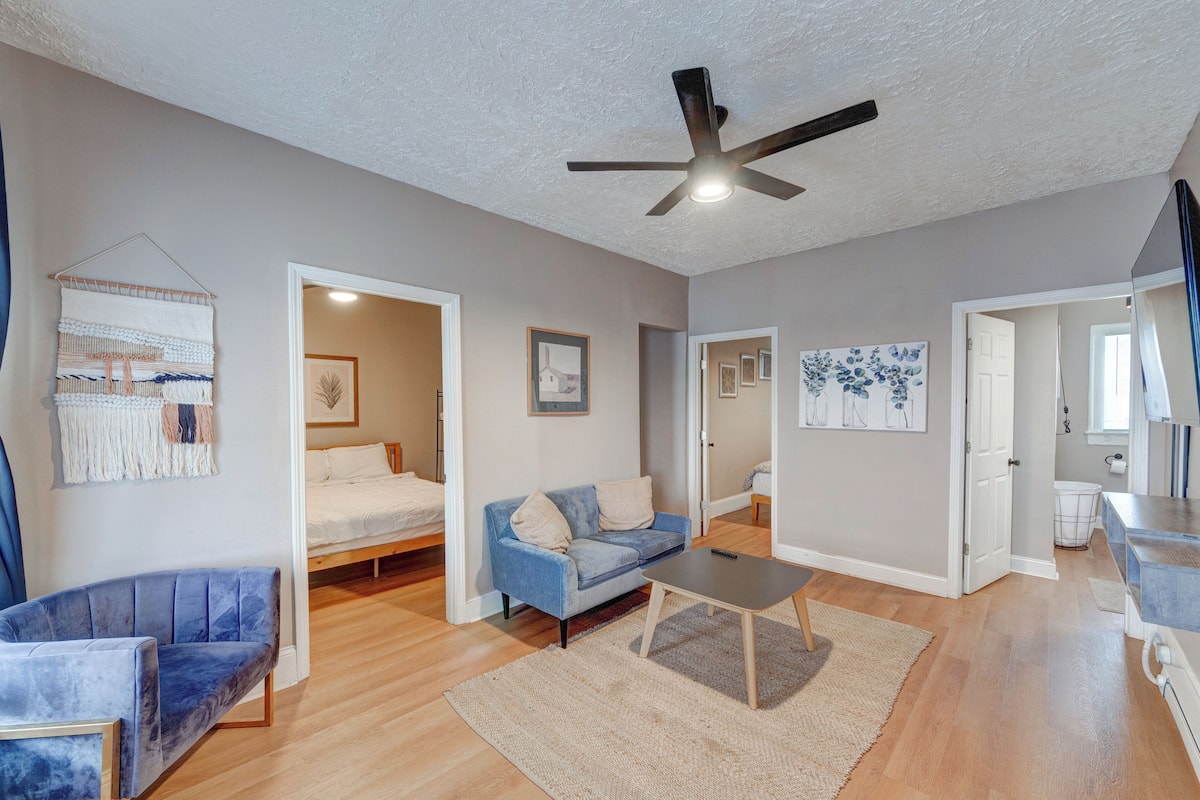 A spacious living room with a blue sofa, a small table, and a ceiling fan.
