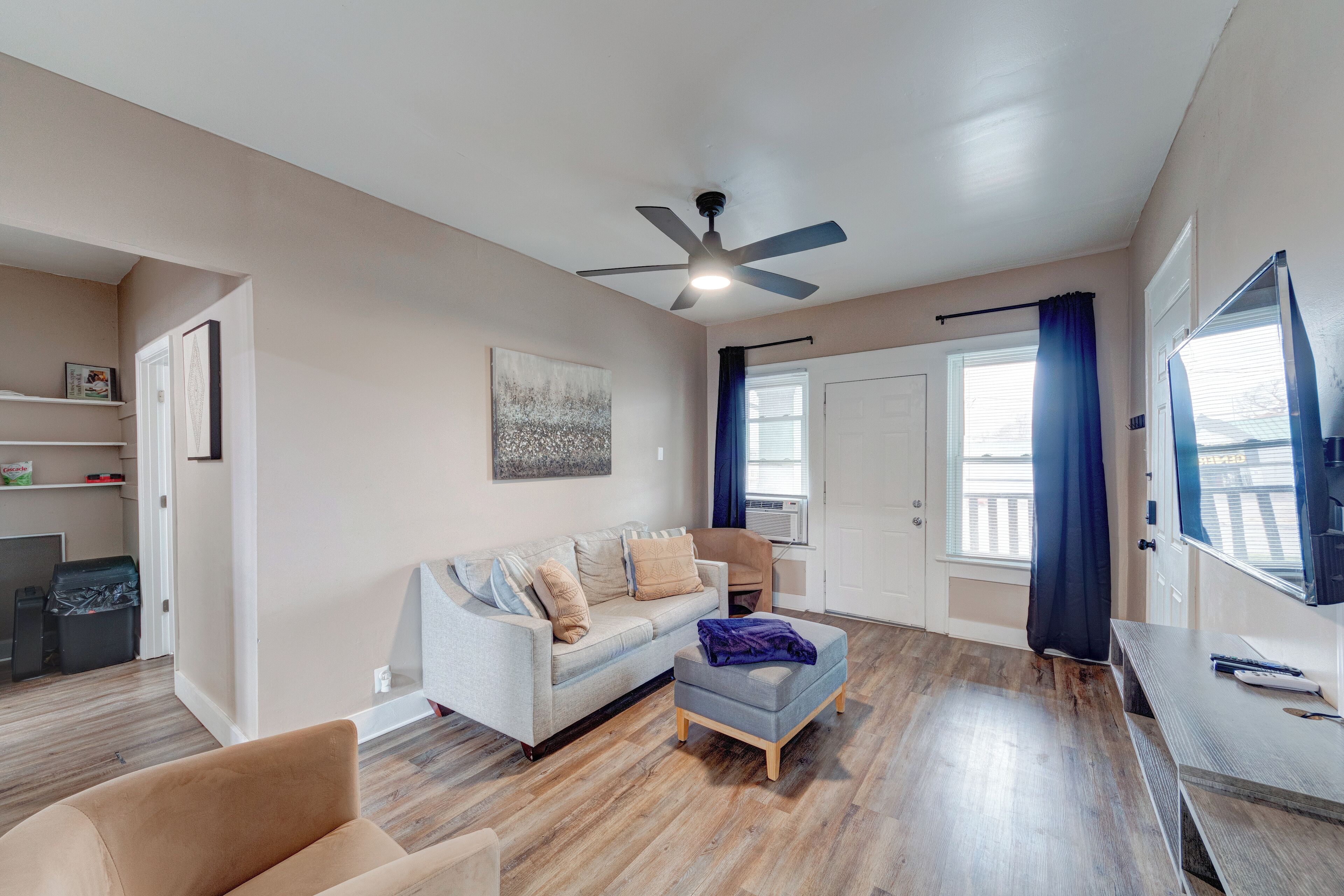 A living room with a sofa, ottoman, ceiling fan, and a TV.