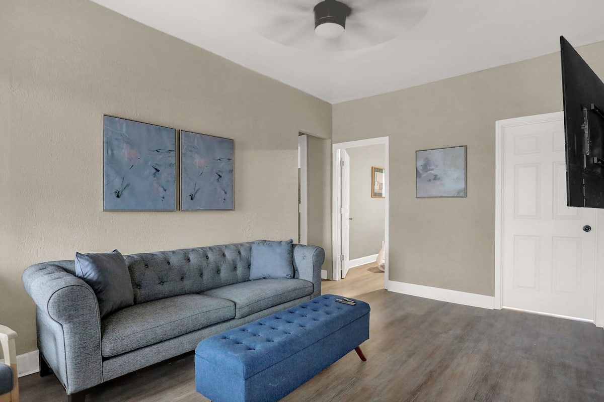 A living room with a grey sofa, a blue ottoman, and two abstract paintings on the wall.