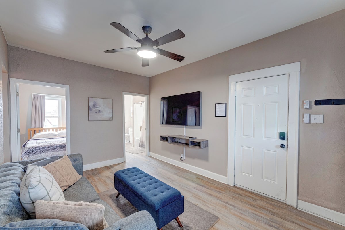 A modern living room with a ceiling fan, a flat-screen TV mounted on the wall, a sofa, and a bench.