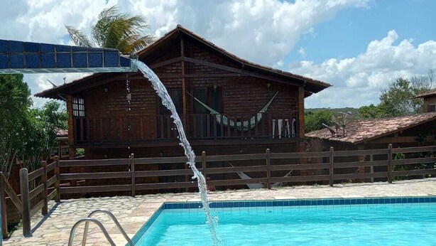 Una piscina con una fuente de agua, un muelle de madera y un edificio con techo de tejas al fondo.