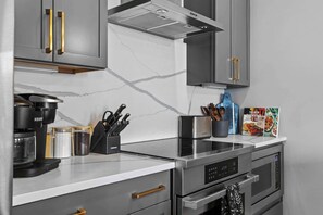 Una cocina moderna con gabinetes grises, una encimera blanca y electrodomésticos de acero inoxidable, incluyendo una cafetera, un tostador y un horno.
