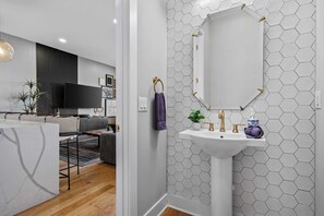 A modern bathroom with a white sink, gold fixtures, and a hexagonal tile backsplash.
