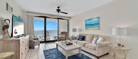 A spacious living room with a large window, a ceiling fan, a sofa, a coffee table, and a TV.