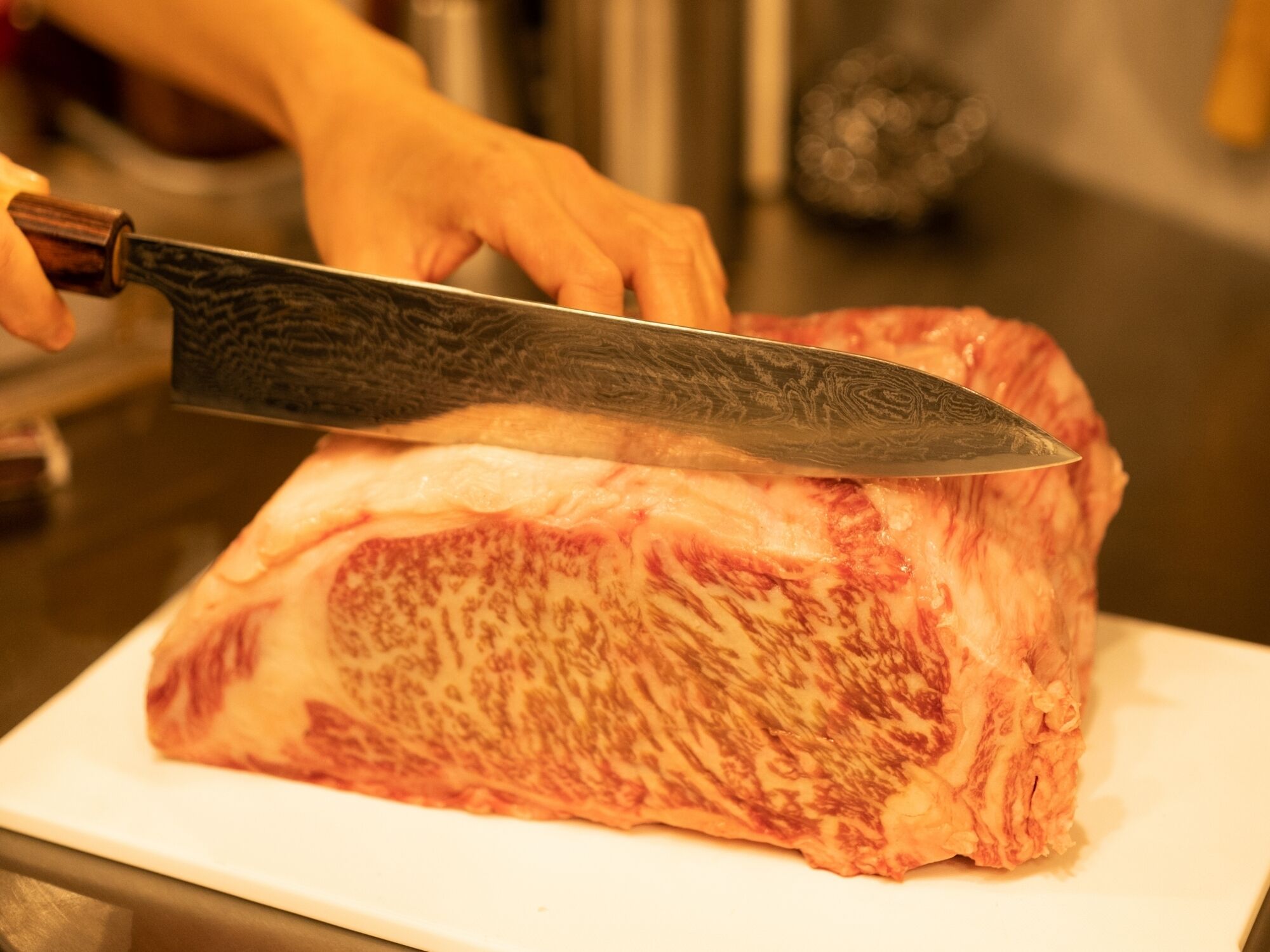 A person using a large knife to cut a piece of meat on a white cutting board.
