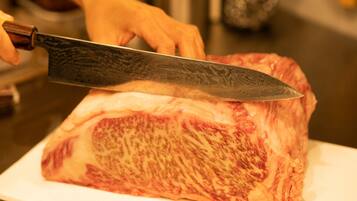 A person using a large knife to cut a piece of meat on a white cutting board.
