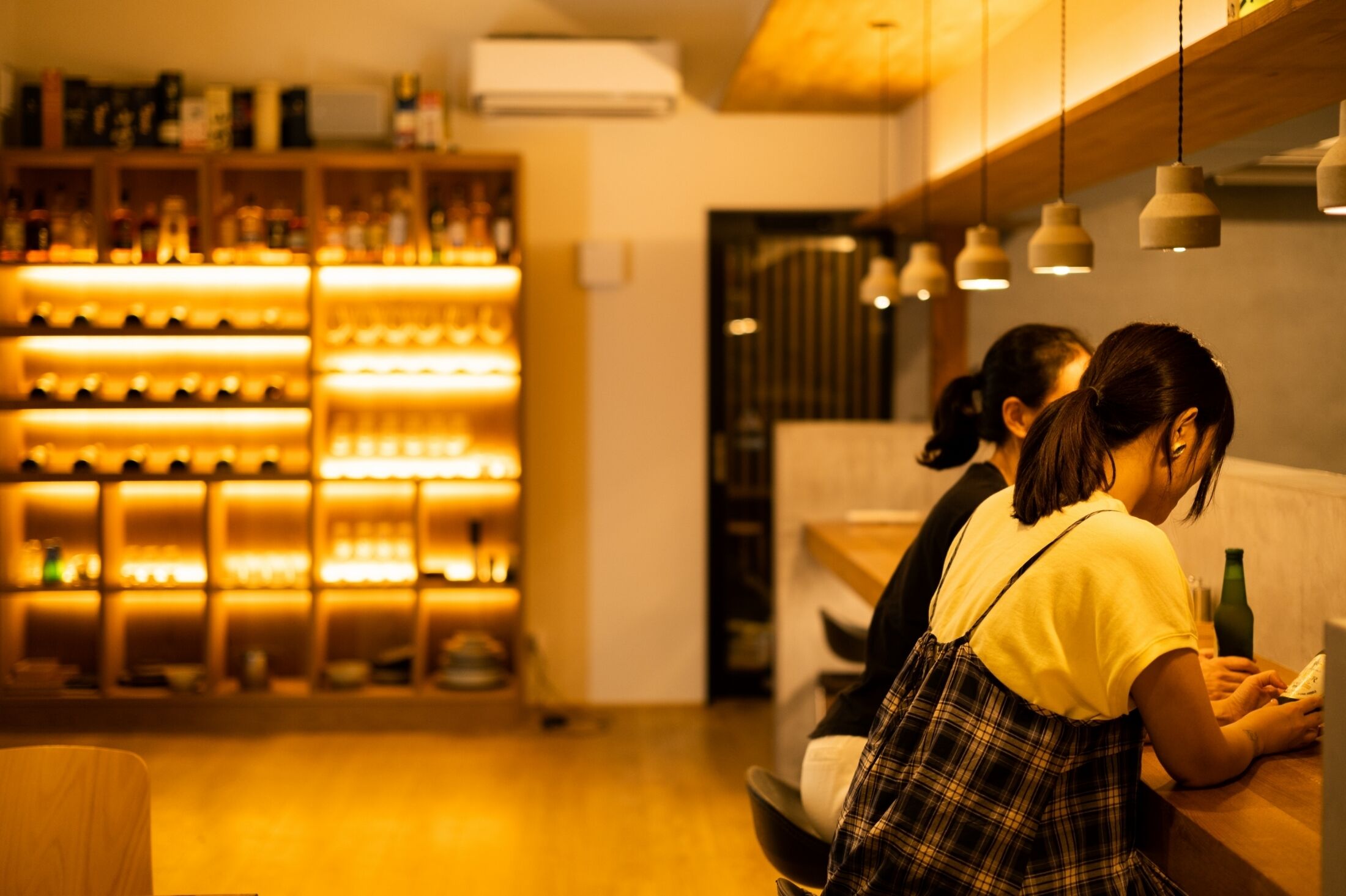 Un espace bar avec des étagères remplies de bouteilles et un comptoir où une personne est assise.
