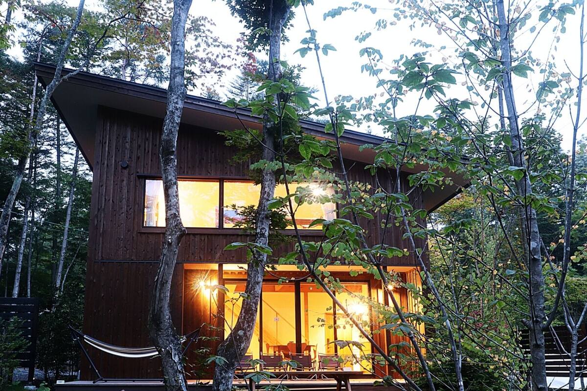 A modern wooden cabin with large windows, surrounded by trees.