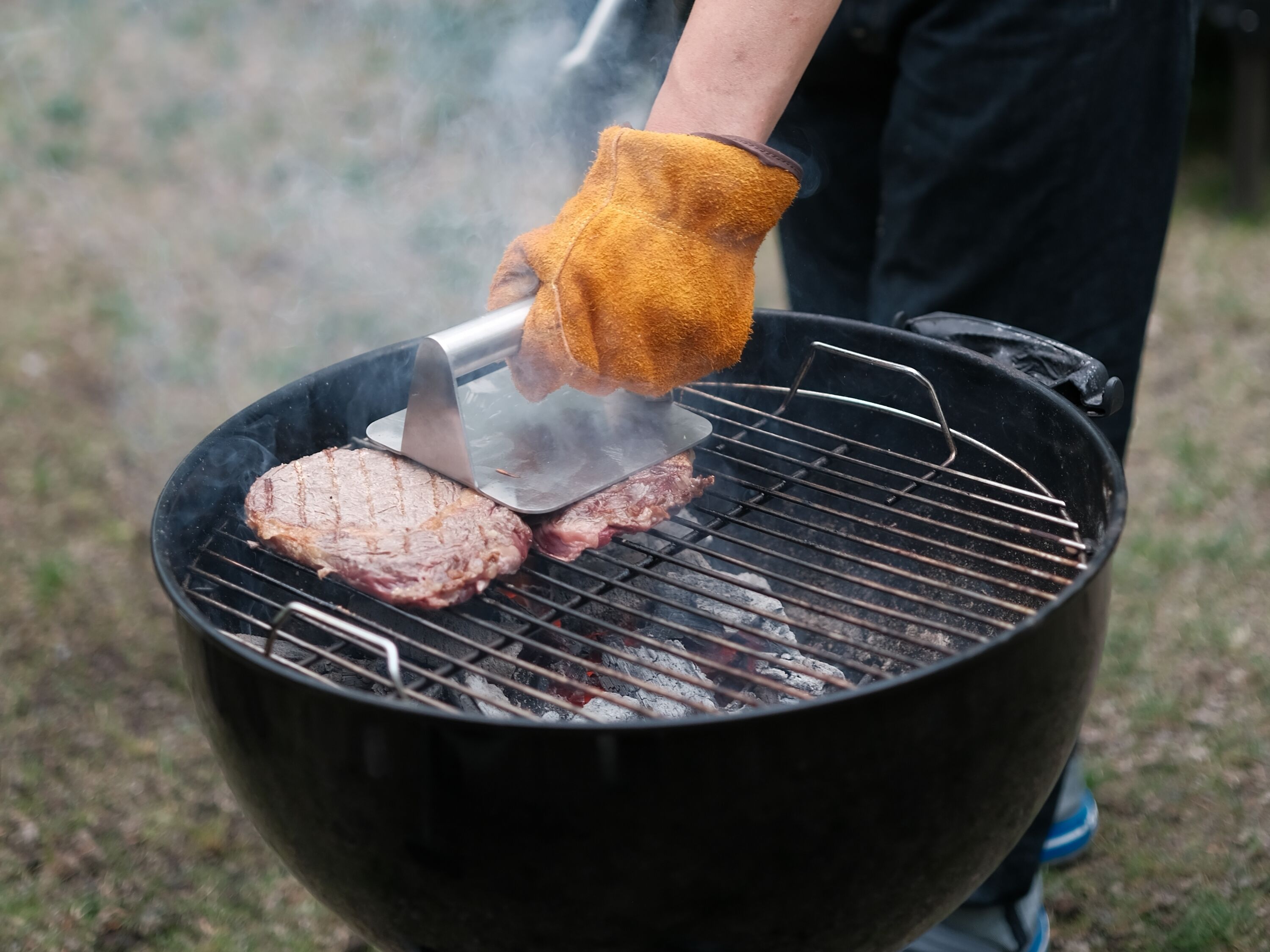 Jemand grillt Steaks auf einem Grill im Freien.