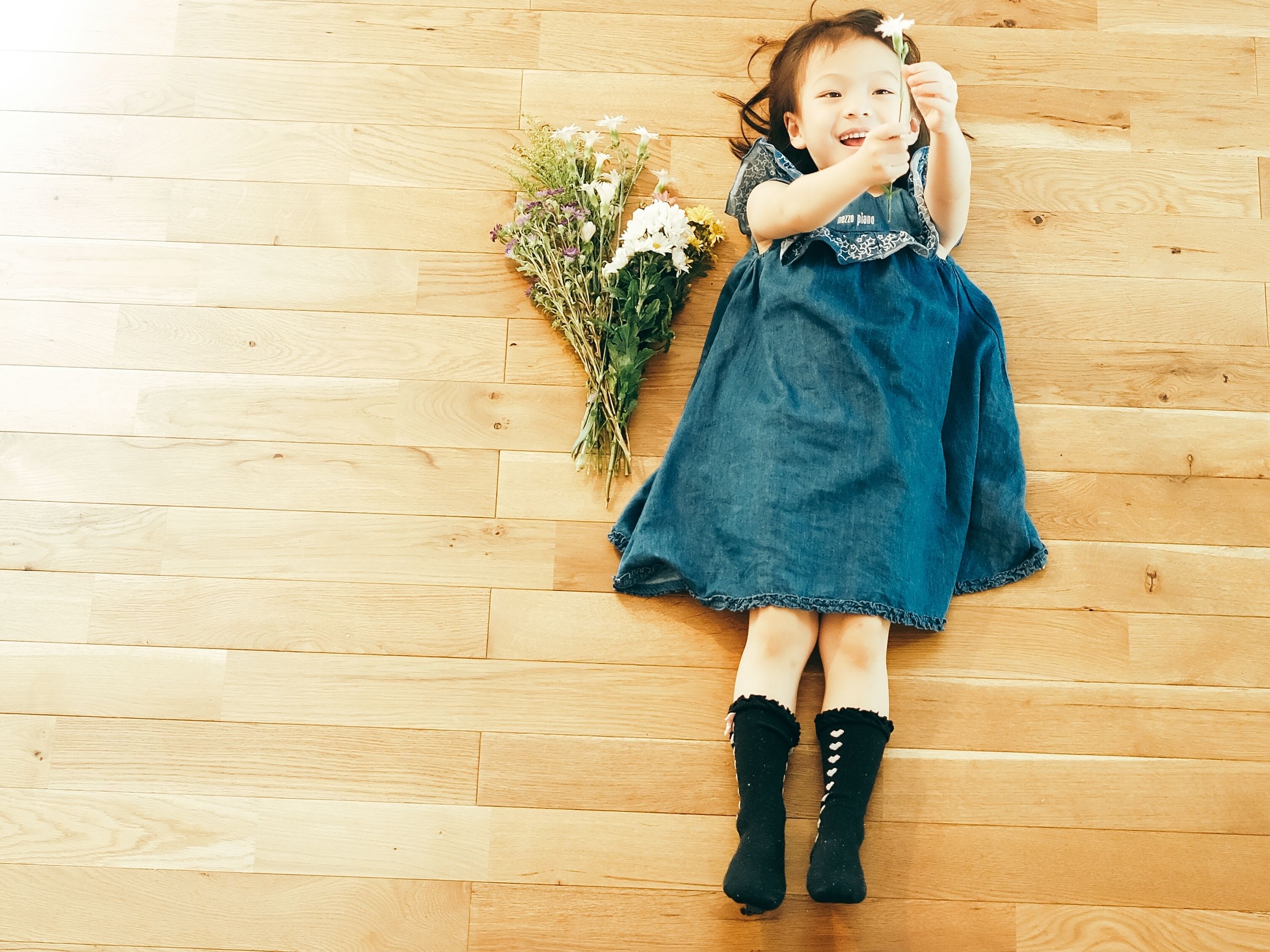 A person lying on a wooden floor with a bouquet of flowers beside them.