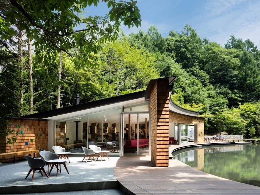 A modern house with a glass facade, wooden deck, and a lake view.